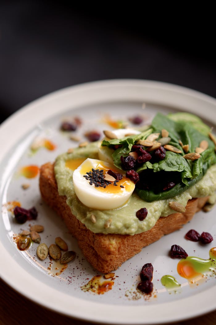 A delectable plate featuring avocado toast with a half-boiled egg, spinach, and seeds.
