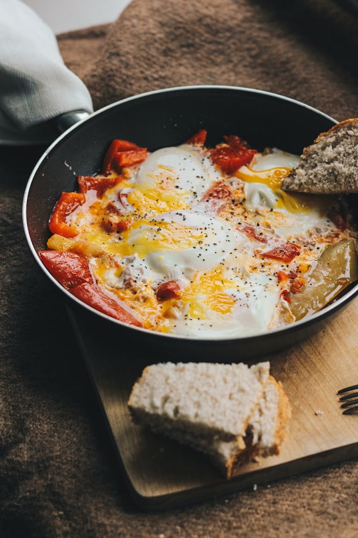 Close-up of homemade shakshuka with tomatoes and eggs served in a pan with bread on the side.